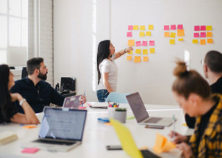 Woman places sticky not on wall containing other sticky notes at a meeting